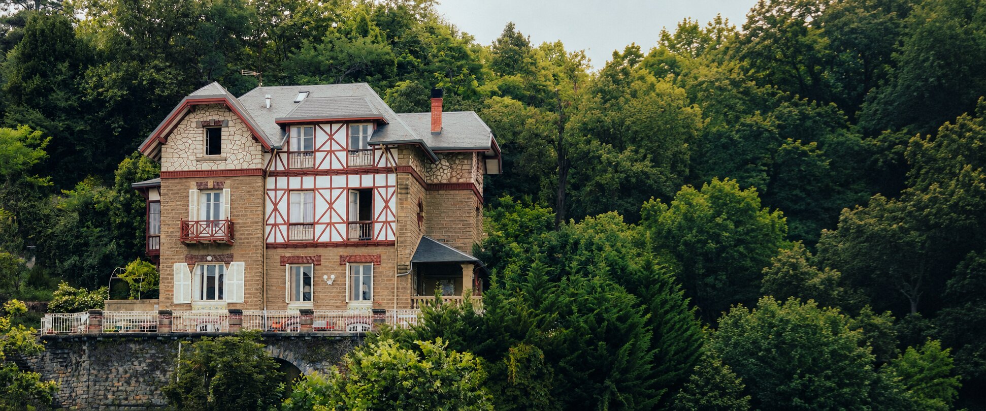 Maison de caractère aux colombages rouges dans un paysage arboré panoramique